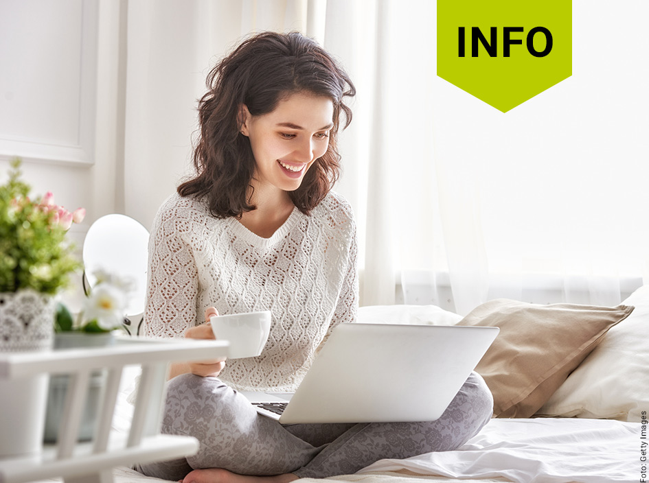 Frau sitzt lächelnd auf dem Sofa und schaut auf ihr Notebook.