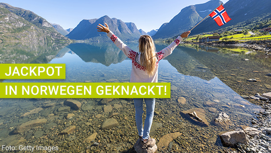 Foto einer Frau, die auf eine schöne Landschaft schaut und die Flagge von Norwegen in die Höhe hält.