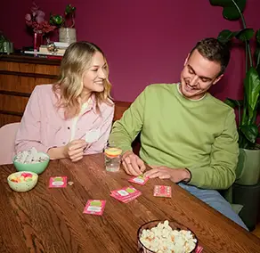Ein junges Paar sitzt am Wohnzimmertisch und rubbelt ein Lucky Bunch auf.