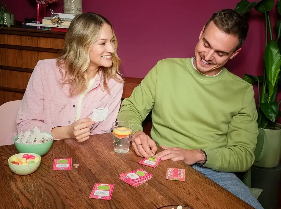 Ein junges Paar sitzt am Wohnzimmertisch und rubbelt ein Lucky Bunch auf.