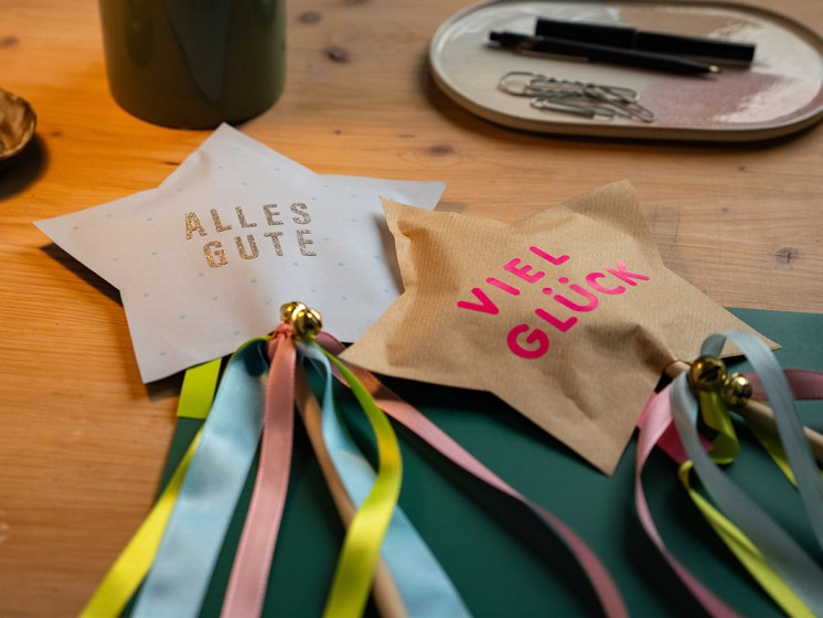 Zwei gebastelte Sterne mit Satinbändern und kleinen Glöckchen an einem Holzstock - WestLotto DIY-Idee