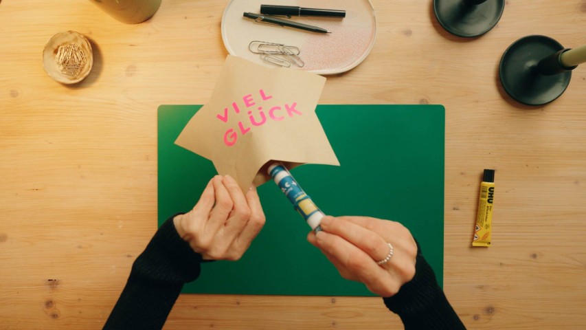 Ein zusammengerolltes GlücksSpirale-Jahreslos wird in zwei zusammengeklebte Sterne aus Kraftpapier gesteckt - WestLotto DIY-Idee