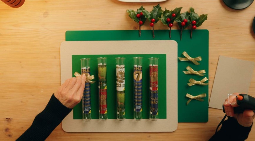 Rubbellos-DIY: Mit WestLotto-Rubbellosen befüllte Glasröhrchen werden mit goldenen Schleifen beklebt
