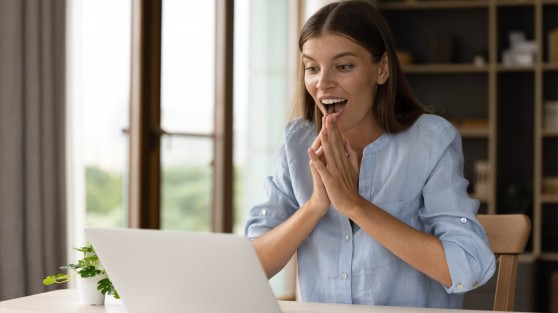Frau sitzt vor Laptop und schaut freudig überrascht | WestLotto Eurojackpot Gewinner