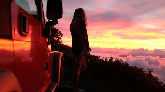 Frau steht auf Berg und schaut sich Sonnenuntergang an. WestLotto