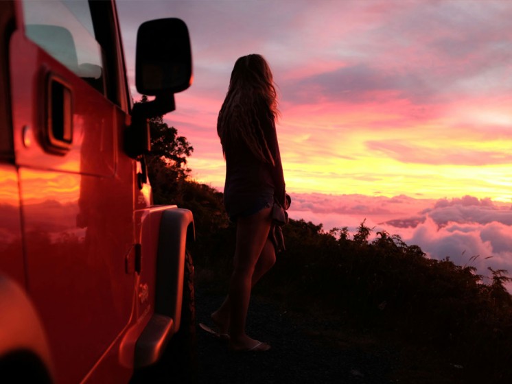 Frau steht auf Berg und schaut sich Sonnenuntergang an. WestLotto