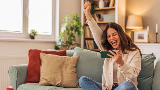 Frau sitzt auf dem Sofa und jubelt - WestLotto Gewinnerbilanz 