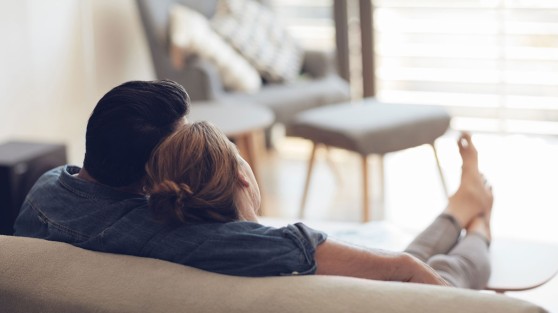 Von hinten fotografiertes Pärchen sitzt auf Couch und schaut aus dem Fenster | Gewinner WestLotto-Rubbellos Mückenjagd