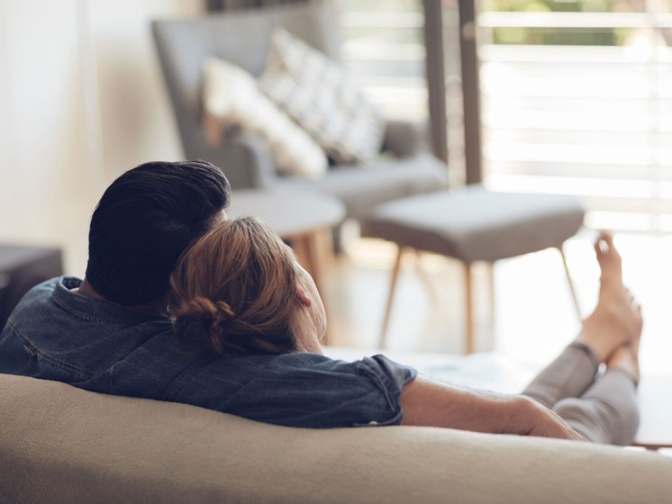 Paar sitzt aus Sofa und schaut aus Fenster. Paar ist nur von hinten zu sehen. | WestLotto Gewinner Rubbellos