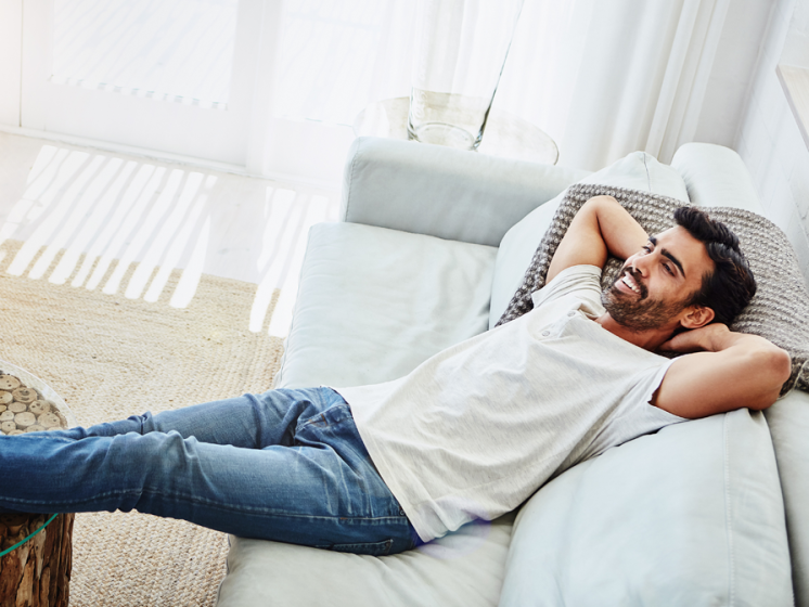 Mann entspannt auf einem grauen Sofa