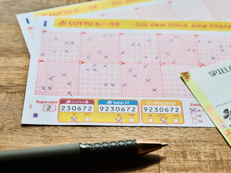 Lotto-Spielscheine und -Quittung liegen auf einem Holztisch. Daneben ein Stift. 