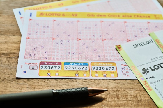 Lotto-Spielscheine und -Quittung liegen auf einem Holztisch. Daneben ein Stift. 