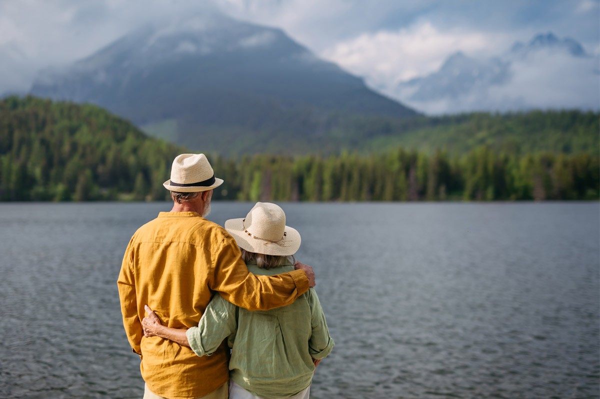 Paar von hinten, welches vor einem See mit Bergkulisse steht - WestLotto Gewinner Rubbellos