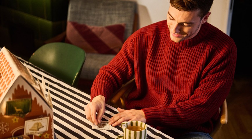 Mann sitzt an weihnachtlich dekoriertem Esstisch und rubbelt ein Rubbellos von WestLotto