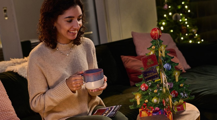 Frau sitzt auf Couch und schaut auf Rubbellos-Adventskalender, der auf kleinem Holztisch steht