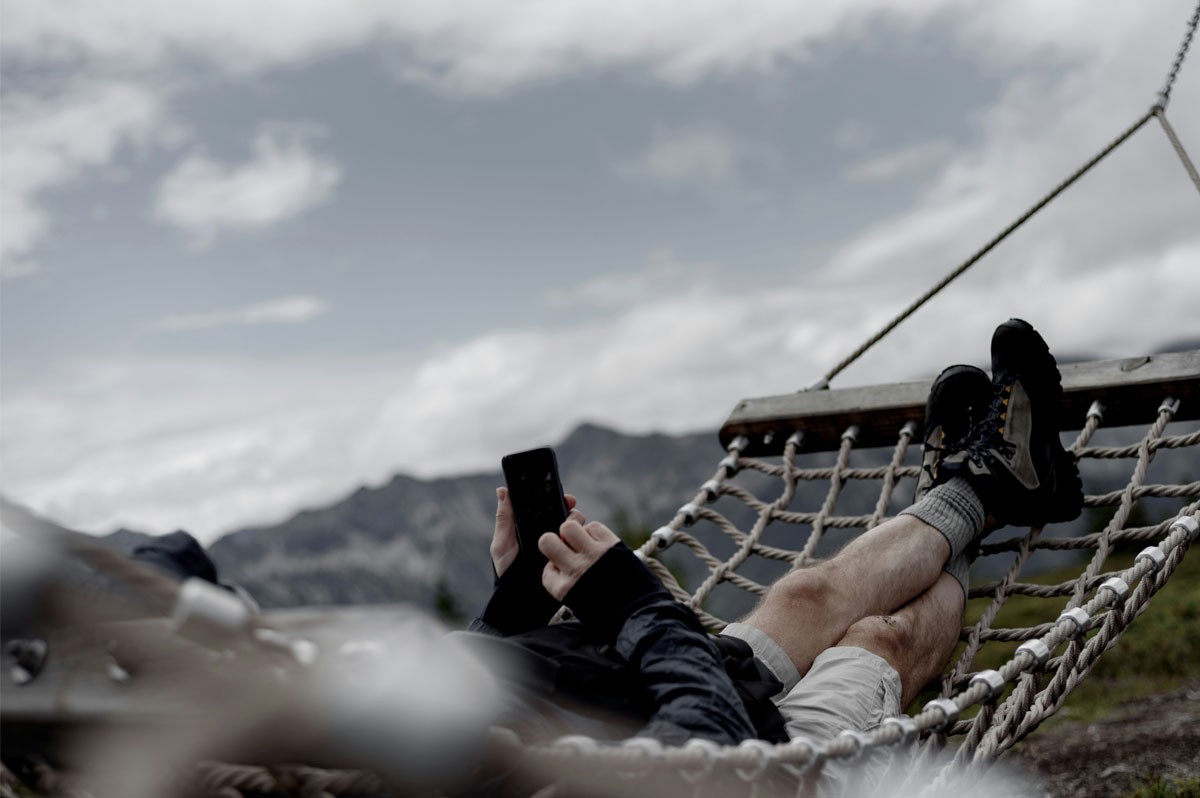 Person liegt in einer Hängematte in den Bergen und bedient sein Smartphone