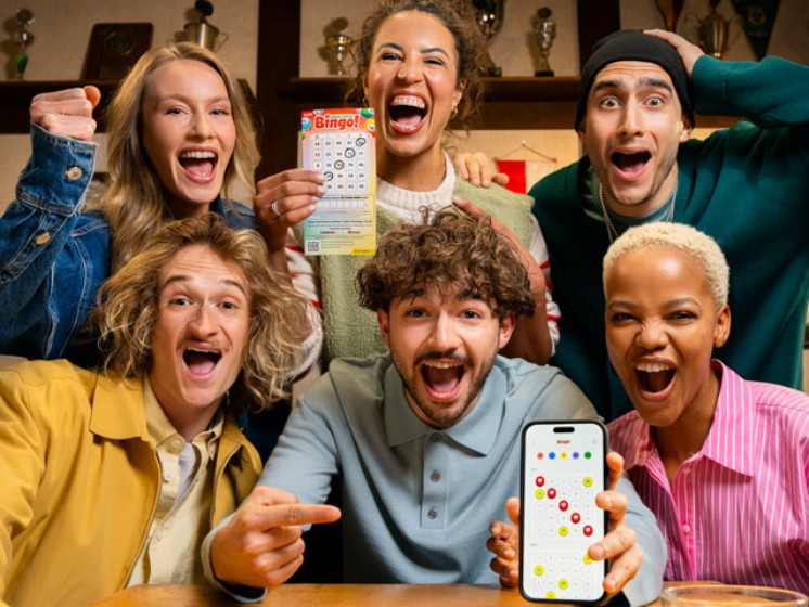 Gruppe von Menschen in einer Kneipe spielen Local Hero Bingo! mit App und Spielschein. WestLotto