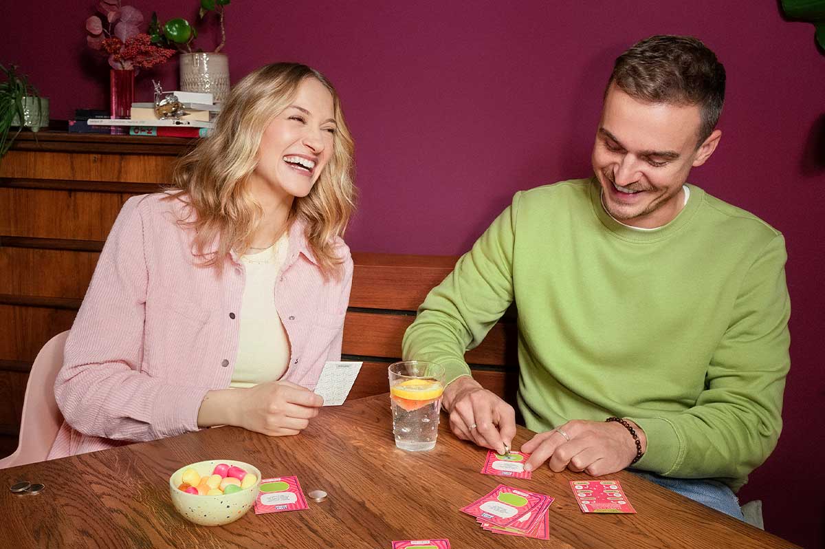 Pärchen sitzt an Esstisch, spielt Rubbelquiz Lucky Bunch und freut sich - WestLotto