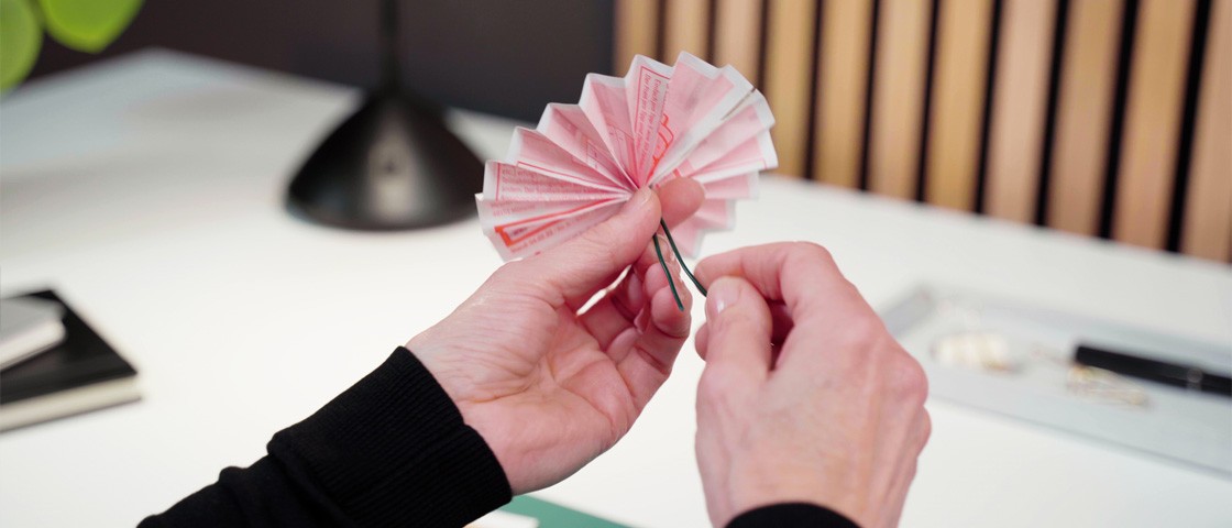 Eine Hand fixiert einen Draht an eine zur Blume gefalteten Eurojackpot-Spielschein | DIY-Idee Lottoschein