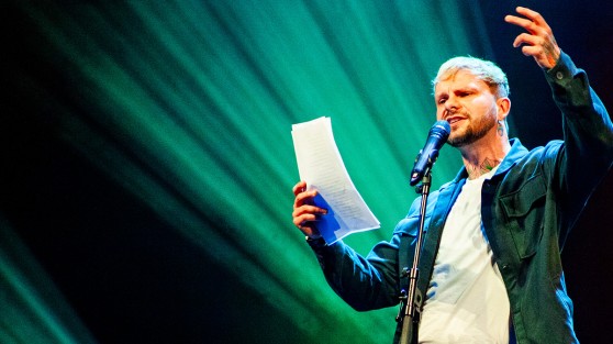 Poetry-Slammer hält Zettel in der Hand und spricht in Mikrofon - WestLotto