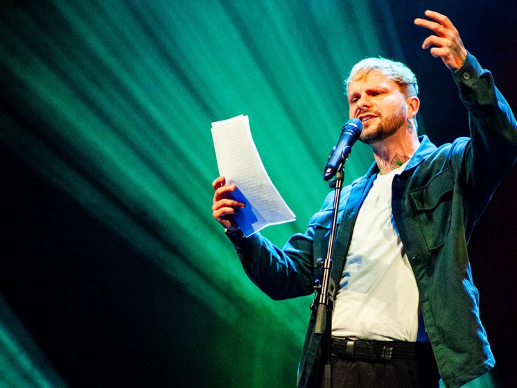 Poetry-Slammer hält Zettel in der Hand und spricht in Mikrofon - WestLotto