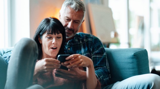 Pärchen sitzt auf Couch und schaut erstaunt auf Smartphone - WestLotto